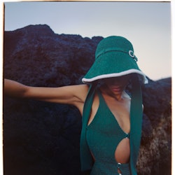 a model wearing a green cutout bathing suit and bucket hat