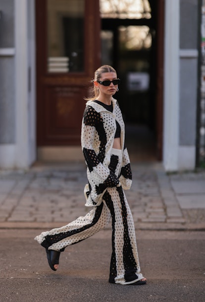 A woman wearing a black and white crochet sweater top and pants.