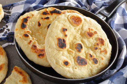 freshly pan fried pita bread in skillet with kitchen towel on concrete table, view from above, close...