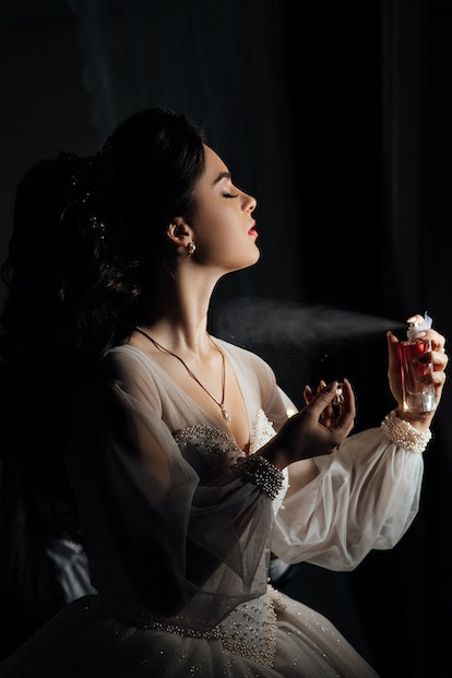 Female beauty. Lovely woman at home. Bride spray perfume stylish woman wearing a white dress spray t...