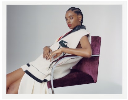 Mereba sitting in a chair while wearing a black-and-white Lacoste vest, and a matching skirt