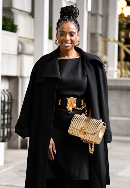 A guest is seen wearing a black coat, black Carolina Herrera dress and gold bag outside the Carolina...