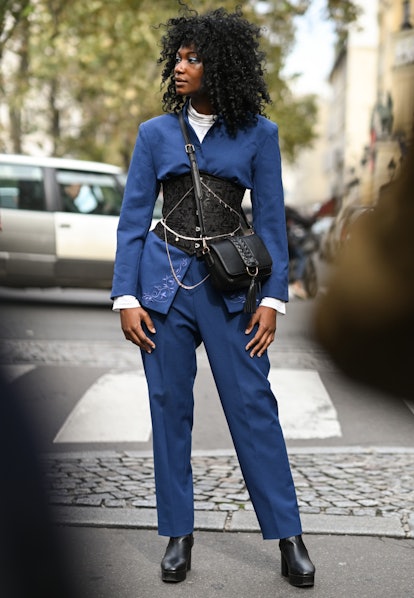 Black corset worn over blue jacket and pants in street style.