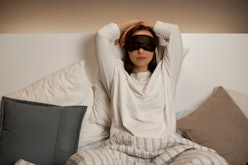 A woman with her hands above her head and a black sleeping mask over her eyes  before sleep