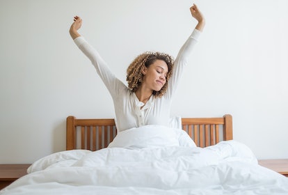 A curly-haired brunette woman stretching her arms after waking up 